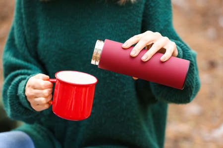 Female tourist with flask drinking hot tea in forest closeup
