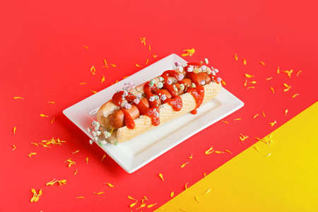 Plate with tasty hot dog and flowers on color background