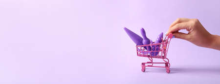 Female hand and shopping cart with sex toys on color backgroundの写真素材