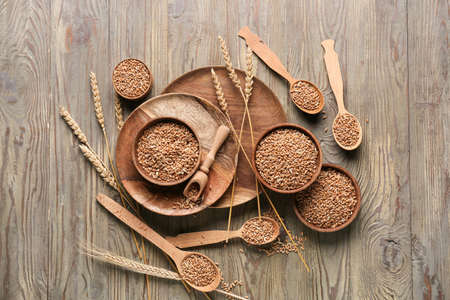 Bowls and spoons with wheat grains on wooden background