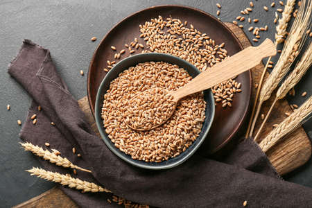 Spoon and bowl with wheat grains on dark background