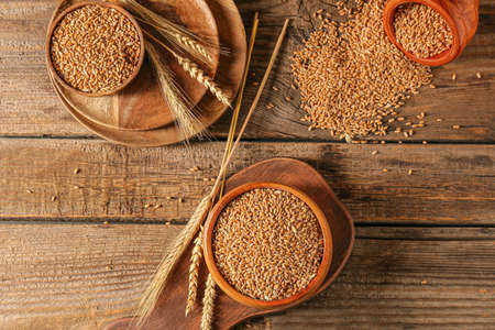 Bowls with wheat grains on color wooden backgroundの写真素材