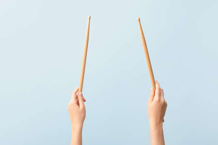 Woman holding wooden drumsticks on color background