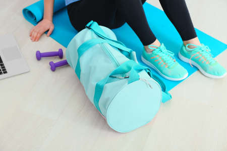 Young woman with sports bag and yoga mat in gym