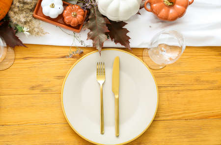 Beautiful table setting with pumpkins and autumn leaves in dining roomの写真素材