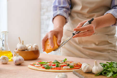 Woman grating cheese on pizza in kitchenの写真素材