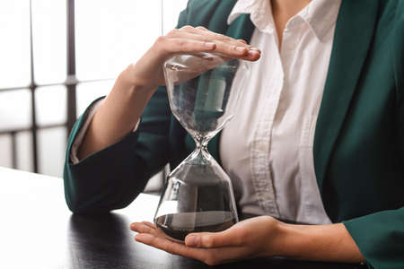 Young businesswoman with hourglass in office, closeupの写真素材
