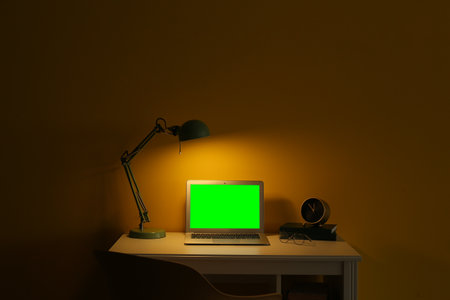 Modern laptop with blank screen at workplace in dark roomの写真素材