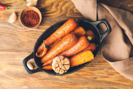 Dish of tasty baked carrot with chili pepper and garlic on wooden backgroundの写真素材