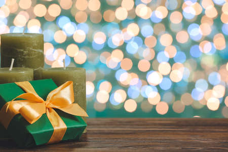 Gift box and candles on wooden table against blurred Christmas lightsの写真素材