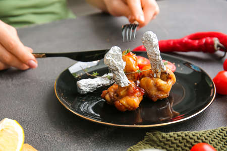 Woman eating tasty chicken lollipops on dark background