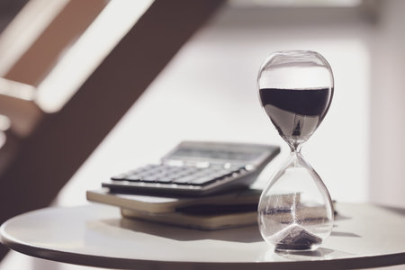 Hourglass, calculator and notebooks on table