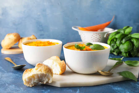 Bowls of fresh carrot cream soup on color backgroundの写真素材