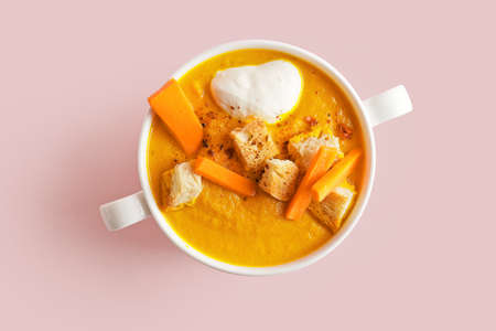 Cooking pot of tasty carrot cream soup on color background