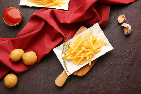Plate with tasty french fries on dark background