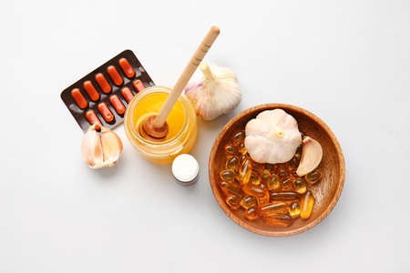 Fresh garlic with honey and pills on light backgroundの写真素材