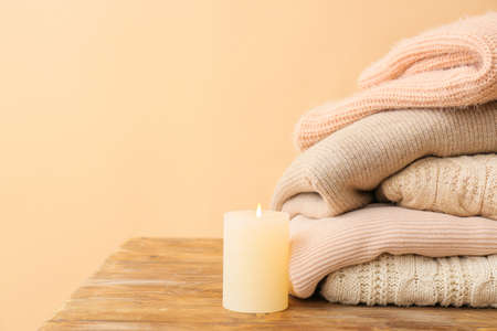 Stylish warm clothes with candle on table against color background