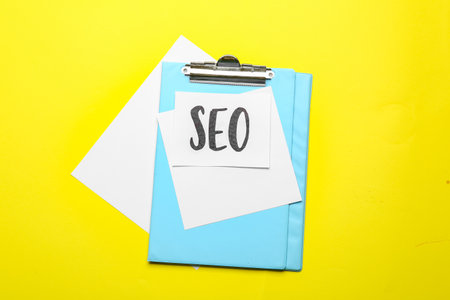 Paper sheet with abbreviation SEO and clipboard on color backgroundの写真素材
