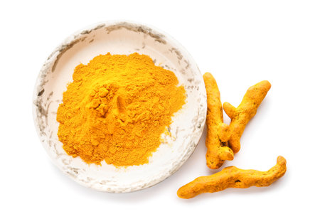 Bowl with turmeric powder and roots on white backgroundの写真素材