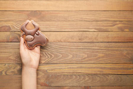 Hand with tasty Christmas cookie in shape of bull on wooden backgroundの写真素材
