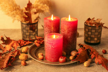 Beautiful aroma candles with autumn leaves on tableの写真素材
