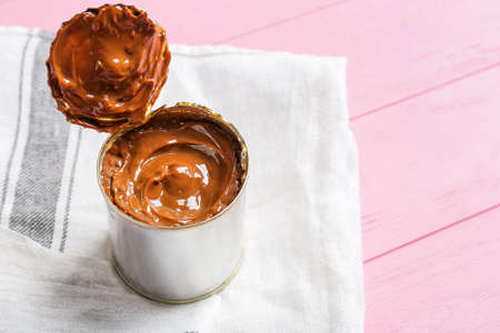 Tin can of boiled condensed milk on color wooden background