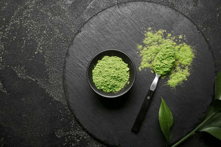 Bowl with powdered matcha tea and spoon on dark background