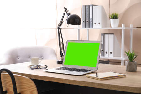 Modern laptop with blank screen at workplace in roomの写真素材