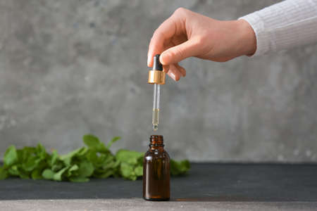 Female hand with bottle of ginger essential oil on dark backgroundの写真素材
