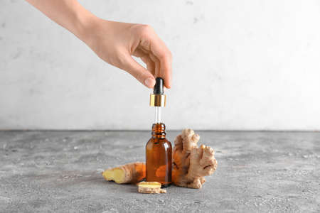Female hand with bottle of ginger essential oil on gray background