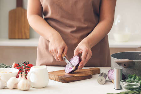 Woman cutting onion on table in kitchenの写真素材