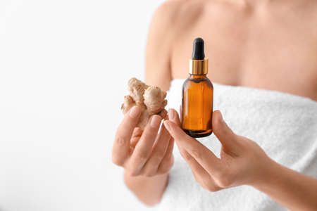 Woman with bottle of ginger essential oil on light backgroundの写真素材
