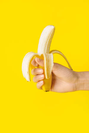 Female hand with tasty ripe banana on color backgroundの写真素材