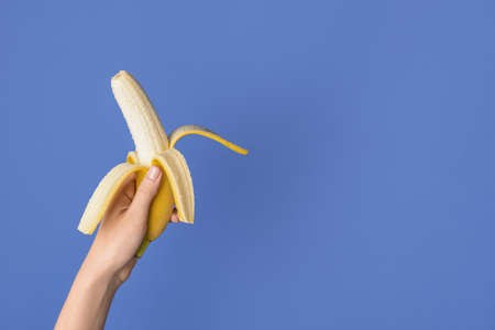 Female hand with tasty ripe banana on color backgroundの写真素材