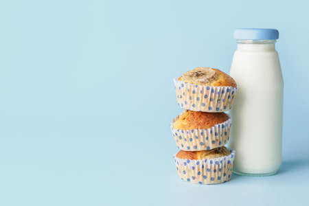 Tasty banana muffins and bottle of milk on color background
