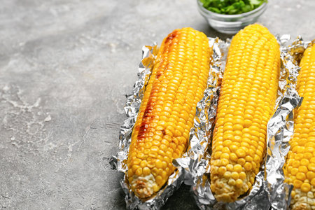 Tasty baked corn cobs on gray background