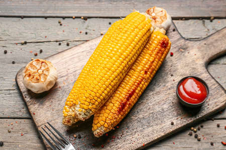 Board with tasty baked corn cobs and garlic on wooden background