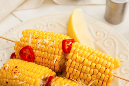 Plate with tasty baked corn cobs on light background