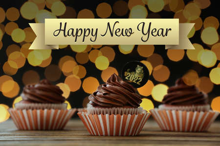 Tasty cupcakes for New Year 2022 celebration on table against blurred lightsの写真素材