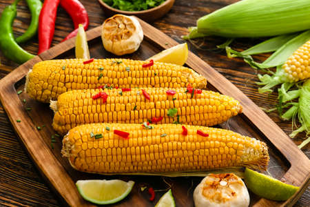 Board with tasty baked corn cobs on wooden backgroundの写真素材