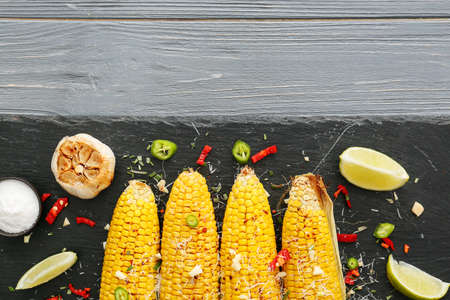 Board with tasty baked corn cobs and garlic on wooden backgroundの写真素材