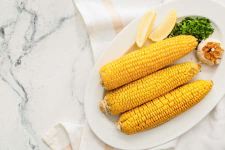 Plate with tasty baked corn cobs on light background