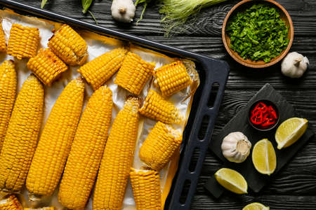 Baking dish with tasty baked corn cobs on dark backgroundの写真素材