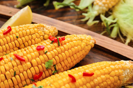 Board with tasty baked corn cobs on wooden backgroundの写真素材