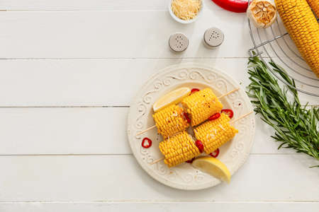 Plate with tasty baked corn cobs on light wooden backgroundの写真素材