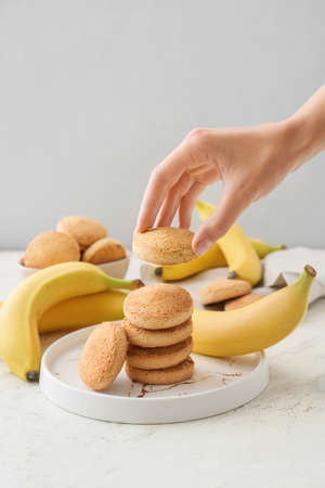Female hand with tasty banana cookies on light backgroundの写真素材