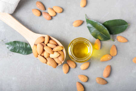 Jar with almond oil and spoon with nuts on gray backgroundの写真素材
