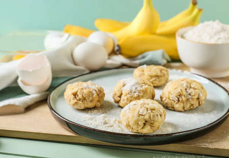 Plate with uncooked banana cookies and ingredients on color wooden backgroundの写真素材