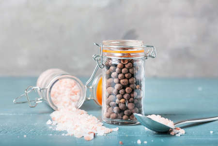 Jars with salt and allspice on color wooden background