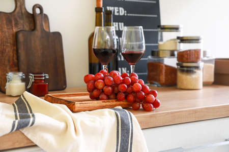 Grapes, glasses of wine and cutting board on kitchen counter
